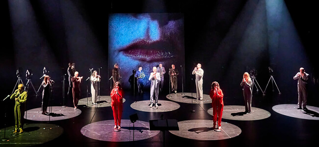 Ein Foto mit Musiker*innen vom Ensemble Modern auf einer Bühne.
Die Musiker*innen stehen einzeln an Mikrofonen.