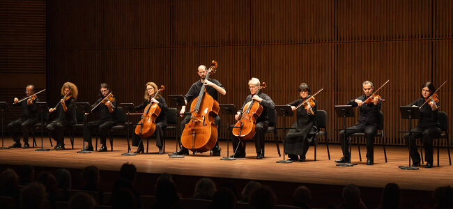 Ein Foto von Musiker*innen vom Ensemble Modern auf einer Bühne.
Die Musiker*innen spielen Streich-Instrumente.
